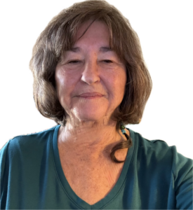 A woman with short, wavy, dark hair smiles warmly at the camera. She is wearing a dark top. She has a woven braid with colorful beads hanging over her shoulder.